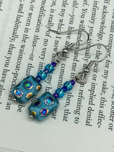 Load image into Gallery viewer, Glass beaded earrings take center stage in this design, with light blue glass beads as the primary color. These beads contain varying shades of blue, purple, and a hint of gold to add interest and texture to the style. As a show-stopping accessory, this piece of jewelry is a must-have for any collection.  Measurements: 1 3/8” in length
