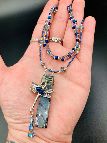 This stunning rectangular-shaped Black Labradorite Stone necklace features a wire-wrapped dragonfly pendant, completed with intricate glass bead detailing. Perfect for a summer night, it will make a bold statement.  Measurements: Necklace is 16” adjustable up to 18