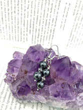 Load image into Gallery viewer, Elevate your boho chic style with these beautiful hematite and glass beaded earrings. Featuring two hematite round beads and a floral silver metal bead in the middle, these earrings offer a stylish and chic touch to any outfit.  Measurements: 1 1/4” in length 
