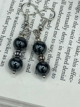 Load image into Gallery viewer, Elevate your boho chic style with these beautiful hematite and glass beaded earrings. Featuring two hematite round beads and a floral silver metal bead in the middle, these earrings offer a stylish and chic touch to any outfit.  Measurements: 1 1/4” in length 
