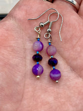 Load image into Gallery viewer, These elegant, glass beaded earrings feature dainty light and dark purple hues, making them a great addition to any summer wardrobe. Perfect for hippie and nature-inspired looks, they are sure to accentuate any style.  Measurements: 1 ” in length
