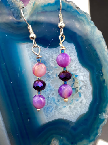 These elegant, glass beaded earrings feature dainty light and dark purple hues, making them a great addition to any summer wardrobe. Perfect for hippie and nature-inspired looks, they are sure to accentuate any style.  Measurements: 1 ” in length