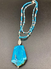 Load image into Gallery viewer, This Vibrant Sea Blue Agate Natural Stone Pendant Choker Style Beaded Necklace includes two strands of glass beads in shades of blues, silver and clear to lend shimmer and color to this large stone pendant. The shorter strand consists of very light blue small glass beads, while the longer strand is primarily a light baby blue. A set of dainty matching earrings completes the look. This beautiful gemstone necklace is the perfect accessory to bring the beach with you in the coming months.
