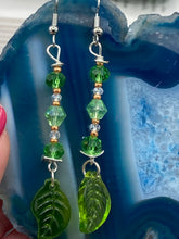 Load image into Gallery viewer, Long strand of glittering light green and gold glass beads, as well as a leaf-shaped glass charm at the bottom, combine to create a highly dynamic effect. These versatile earrings, perfect for a whimsical fairy princess, good witch, or nature-loving hippie look, draw on nature-inspired designs, providing the ideal finishing touch to any ensemble.  Measurements: 2 1/4” in length
