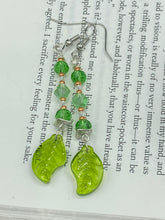 Load image into Gallery viewer, Long strand of glittering light green and gold glass beads, as well as a leaf-shaped glass charm at the bottom, combine to create a highly dynamic effect. These versatile earrings, perfect for a whimsical fairy princess, good witch, or nature-loving hippie look, draw on nature-inspired designs, providing the ideal finishing touch to any ensemble.  Measurements: 2 1/4” in length

