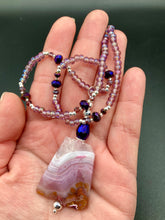 Load image into Gallery viewer, A soft dusty rose agate pendant is accompanied by shimmery beads of dusty rose, blue, dark pink, and gold. Adorned with large deep purple glass beads with a hint of gold shimmer, this stunning necklace set evokes a rose garden.  Measurements:  Necklace is 15” adjustable to 18&quot;
