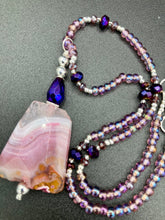 Load image into Gallery viewer, A soft dusty rose agate pendant is accompanied by shimmery beads of dusty rose, blue, dark pink, and gold. Adorned with large deep purple glass beads with a hint of gold shimmer, this stunning necklace set evokes a rose garden.  Measurements:  Necklace is 15” adjustable to 18&quot;
