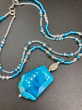 Load image into Gallery viewer, This Vibrant Sea Blue Agate Natural Stone Pendant Choker Style Beaded Necklace includes two strands of glass beads in shades of blues, silver and clear to lend shimmer and color to this large stone pendant. The shorter strand consists of very light blue small glass beads, while the longer strand is primarily a light baby blue. A set of dainty matching earrings completes the look. This beautiful gemstone necklace is the perfect accessory to bring the beach with you in the coming months.
