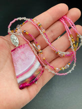 Load image into Gallery viewer, This large agate pendant features a variety of pink hues, from light to dark, and is accompanied by two strands of glass beaded necklaces with pink, silver, gold, and clear beads. The combination of colors creates a stunning and vibrant look, perfect for accessorizing any summer look.  Measurements:  Necklace is 15” adjustable up to 18&quot; in length 
