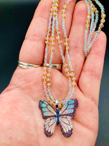 This precious sterling silver pendant features a hand-crafted butterfly whose wings have been artistically molded from a basil leaf and painted in a trio of light blue, silver, and gold hues. Accompanying the butterfly pendant are two glass beaded necklaces in an alluring combination of light blue, gold, and medium-small clear glass beads. A stunning summer accessory.  Measurements:  Necklace is 16” adjustable up to 18