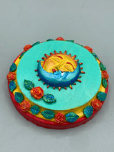 Load image into Gallery viewer, Handcrafted polymer clay wall art with a wood frame, featuring a sun and moon motif complemented with contrasting cool and warm colors. The background is a bright turquoise hue, with marigold flowers and leaves adorning the frame.Measurement 4&quot; diameter
