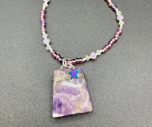 This sophisticated trapezoid-shaped wired amethyst pendant featuring a hematite star bead provides a unique, star-studded night sky look. Multicolored glass beads in shades of pink, purple, blue and gold feature along a single-stranded necklace, intermixed with larger, soft dusty rose glass beads and iridescent beads for a subtle shimmer. Necklace is 17