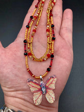 Load image into Gallery viewer, This intricately crafted pendant features a Basil leaf molded in Sterling Silver and adorned with stunningly vivid red, gold, and black glass beaded necklace. Its eye-catching butterfly design adds a bold, yet whimsical touch, making it an ideal choice for a summer look. Necklace is 15 1/2” in length adjustable to 18&quot;
