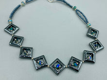 Load image into Gallery viewer, This two-strand necklace, crafted from aqua-blue and silver toned glass beads, is a stunning statement piece. The addition of faceted triangle-shaped glass beads tucked between hematite square beads adds an exquisite and unique flair. The necklace gracefully drapes around the neck, bringing an air of bold and elegant flair to any ensemble it complements. 15” in length, can be extended up to 17"
