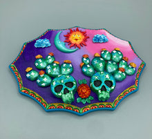 Load image into Gallery viewer, This handcrafted polymer clay wall art features a wood frame painted in a gradient from light pink to dark purple, creating a stunning sunset look. With two bright green skull cactus plant and bright yellow orange blooming flowers. Featuring a vivid sun and crescent moon with a backdrop of dark blue clouds, this frame is sure to make an impression. A bight teal and yellow hue frame to make a bold contrast with the warm background hue. This piece is sure to make a statement.
