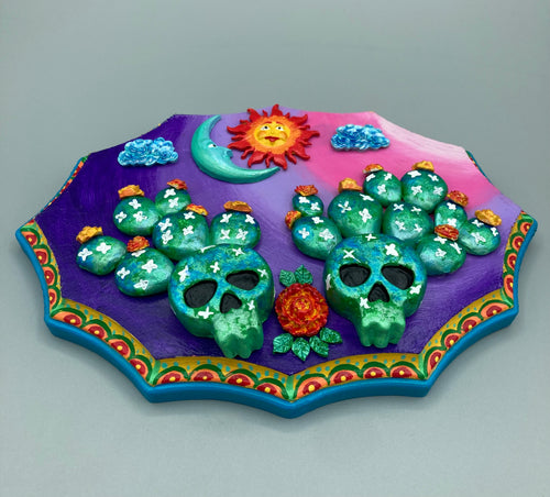 This handcrafted polymer clay wall art features a wood frame painted in a gradient from light pink to dark purple, creating a stunning sunset look. With two bright green skull cactus plant and bright yellow orange blooming flowers. Featuring a vivid sun and crescent moon with a backdrop of dark blue clouds, this frame is sure to make an impression. A bight teal and yellow hue frame to make a bold contrast with the warm background hue. This piece is sure to make a statement.