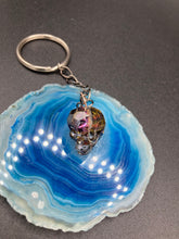 Load image into Gallery viewer, This beautiful edgy gun metal faceted shimmery multi-color glass skull bead keychain is full of hues of silver, purple, pink, blue, and gold. The split nickel key ring is 1 1/4&quot; in diameter and the entire key chain is 4 1/2&quot; in length (from key ring to skull bead)  Measurements: Nickel Free Key Ring is 1 1/4” in diameter, Entire Key Chain is 4 1/2&quot; in Length, Metal Skull Bead 5/8&quot; in Height
