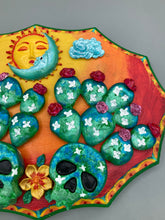 Load image into Gallery viewer, This handcrafted polymer clay wall art features a wood frame painted in a gradient from light yellow to dark red, creating a stunning sunset look. With two bright green skull cactus plant and bright dark red blooming flowers. Featuring a vivid sun and crescent moon with a backdrop of light blue clouds, this frame is sure to make an impression. A bight green hue frame to make a bold contrast with the warm background hue. This piece is sure to make a statement.
