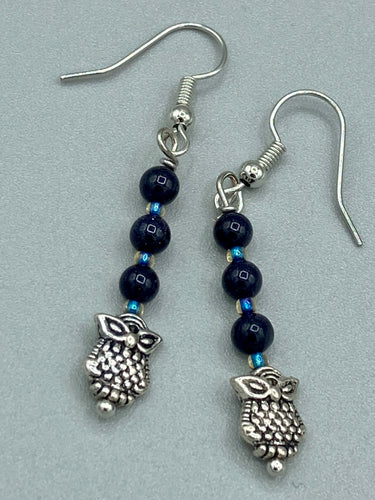 Showcasing shimmery purple goldstone beads, these classy silver-plated owl charm earrings make a statement.  Measurements: 1 3/16” in length