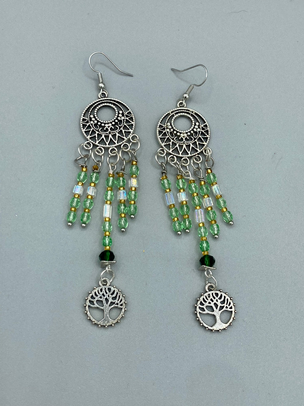 Be mesmerized by these large cascade style earrings, featuring five delicate strands of light green, iridescent and gold-tone beads with a tree of life charm for an eye-catching effect. Perfect for whimsical, nature-inspired looks, these earrings will liven up any outfit.  Measurements: 3 3/4” in length 