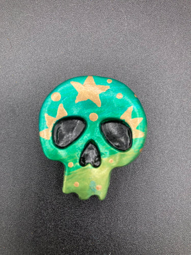 Ideal magnet design to adorn your refrigerator, lockers, workstation, toolbox, or dishwasher. Featuring intricate details and vibrant colors, this hand-painted skull statuette is inspired by nature. Its warm metallic green and gold hues recall the gorgeous tansy beetle, and the addition of moon and stars silhouettes creates a complete celestial motif.  H 1 1/2” x W 1 1/2” x D 3/4”