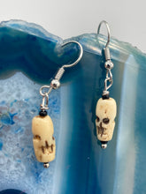 Load image into Gallery viewer, This set of earrings features mini bone-carved skull beads set in black glass. Perfect for goth, emo, witchy or Day of the Dead ensembles, these earrings will bring a unique flair to any outfit.   Measurements: 1 ” in length  
