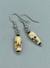 Load image into Gallery viewer, This set of earrings features mini bone-carved skull beads set in black glass. Perfect for goth, emo, witchy or Day of the Dead ensembles, these earrings will bring a unique flair to any outfit.   Measurements: 1 ” in length  
