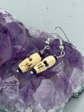 Load image into Gallery viewer, This set of earrings features mini bone-carved skull beads set in black glass. Perfect for goth, emo, witchy or Day of the Dead ensembles, these earrings will bring a unique flair to any outfit.   Measurements: 1 ” in length  
