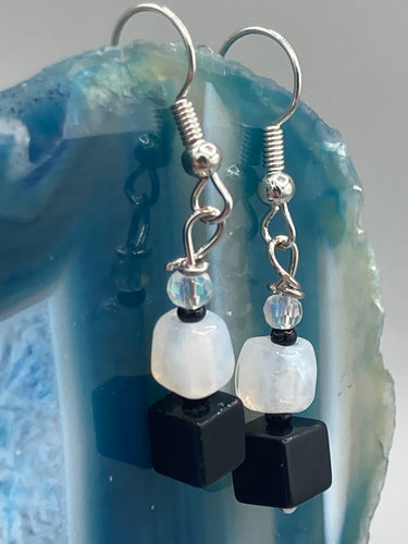 Featuring a large square-shaped black obsidian bead with iridescent glass accents, these earrings boast an intriguing, yet versatile aesthetic. Measurements: 1” in length