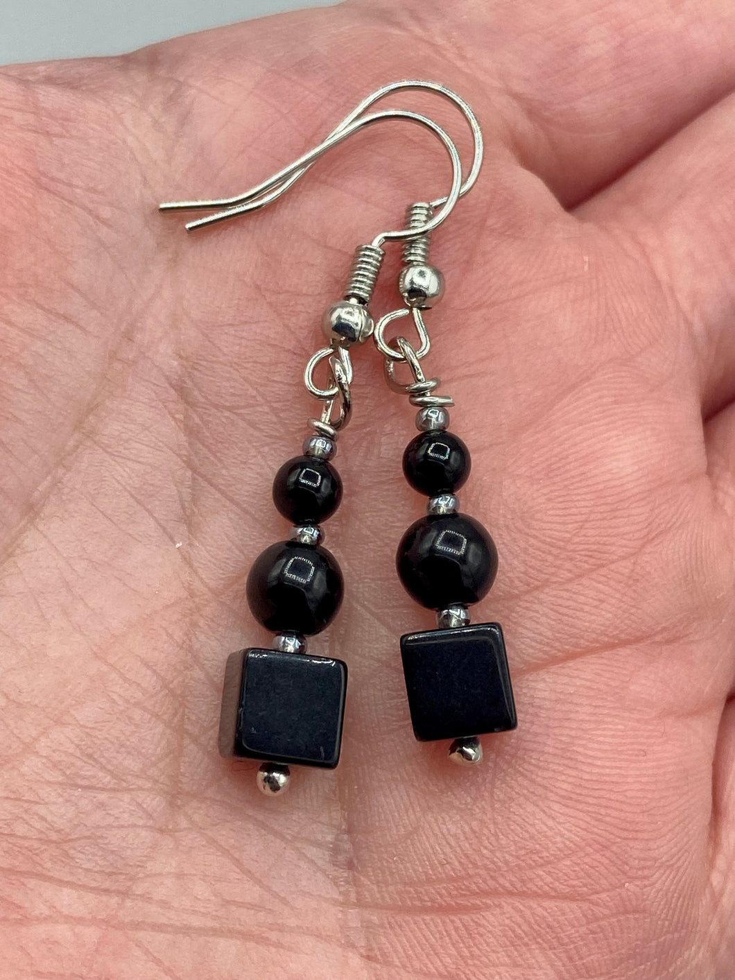 These earrings are crafted with large square-shaped black obsidian beads and small round-shaped black obsidian beads, paired with light gray glass beads. This combination provides an eye-catching, yet versatile look. Measurements: 1” in length