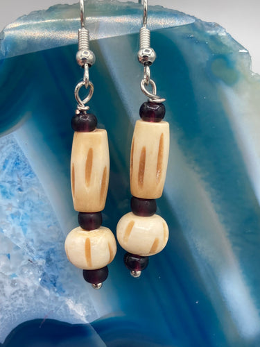 This classic set of earrings is crafted with a combination of cylindrical and round bone beads and dark burgundy glass beads. Offering subtle versatility with its neutral colors, it can easily dress up or dress down any look for a distinct, unique style.  Measurements: 1 5/8 ” in length  