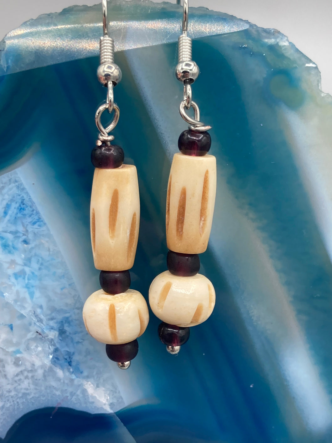 This classic set of earrings is crafted with a combination of cylindrical and round bone beads and dark burgundy glass beads. Offering subtle versatility with its neutral colors, it can easily dress up or dress down any look for a distinct, unique style.  Measurements: 1 5/8 ” in length  