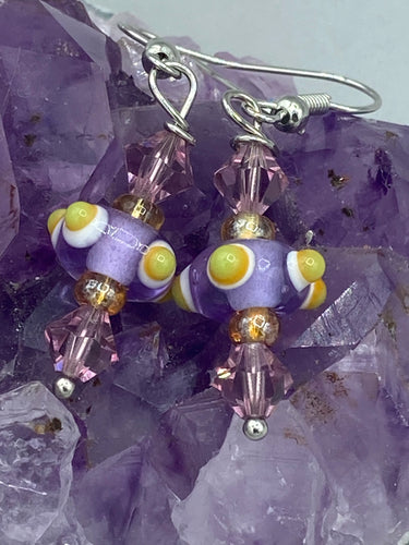 Marvel at the vivid colored bumpy round lampworked glass beads in this earring set, ranging from soft purple to yellow and white. Get creative and imagine the fiesta piñata-shaped bead as a virus for a unique, one-of-a-kind look. Crafted with care and full of personality, this jewelry will be sure to make a statement. Measurements: 1 1/4” in length