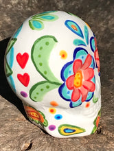 Load image into Gallery viewer, Inspired by nature, this ceramic skull statuette is full of vibrant color and intricate details. The primary color is white with multi-color floral motifs that are painted across the 

