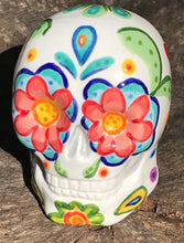Load image into Gallery viewer, Inspired by nature, this ceramic skull statuette is full of vibrant color and intricate details. The primary color is white with multi-color floral motifs that are painted across the 
