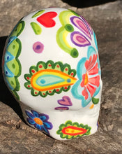 Load image into Gallery viewer, Inspired by nature, this ceramic skull statuette is full of vibrant color and intricate details that I hand painted. The primary color is white with multi-color floral motifs that are painted across the skull, along with hearts and leaves and lively colorful accents around the entire skull. 
