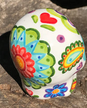 Load image into Gallery viewer, Inspired by nature, this ceramic skull statuette is full of vibrant color and intricate details that I hand painted. The primary color is white with multi-color floral motifs that are painted across the skull, along with hearts and leaves and lively colorful accents around the entire skull. 
