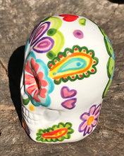 Load image into Gallery viewer, Inspired by nature, this ceramic skull statuette is full of vibrant color and intricate details that I hand painted. The primary color is white with multi-color floral motifs that are painted across the skull, along with hearts and leaves and lively colorful accents around the entire skull. 
