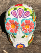 Load image into Gallery viewer, Inspired by nature, this ceramic skull statuette is full of vibrant color and intricate details that I hand painted. The primary color is white with multi-color floral motifs that are painted across the skull, along with hearts and leaves and lively colorful accents around the entire skull. 
