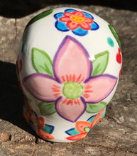 Load image into Gallery viewer, Inspired by nature, this ceramic skull statuette is full of vibrant color and intricate details. The primary color is white with multi-color floral motifs that are painted across the skull, along with hearts and leaves and lively colorful accents around the entire skull.
