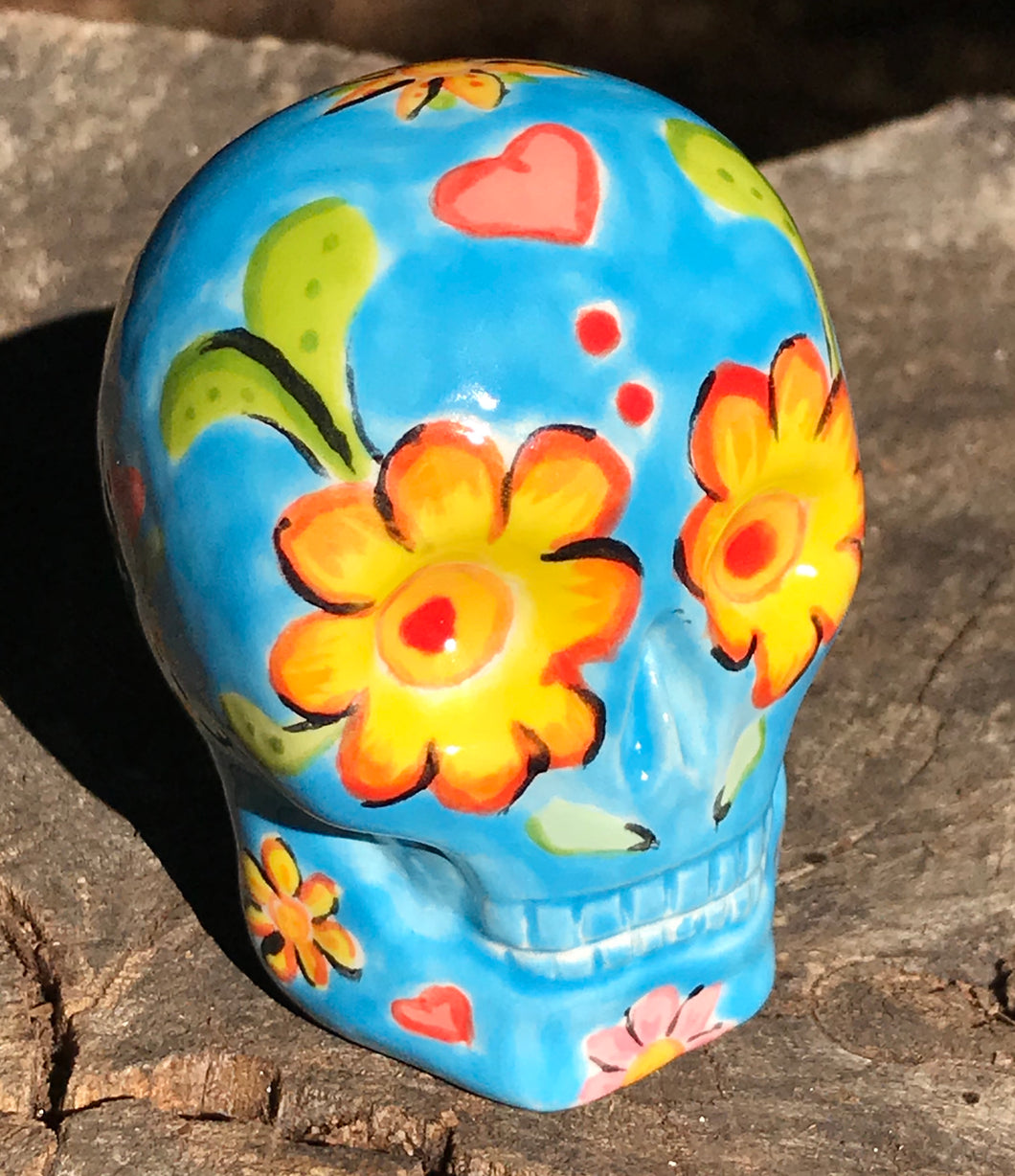 Inspired by nature, this ceramic skull statuette is full of vibrant color and intricate details. The primary color is blue with multi-color floral motifs that are painted across the skull, along with hearts and leaves and lively colorful accents around the entire skull. 
