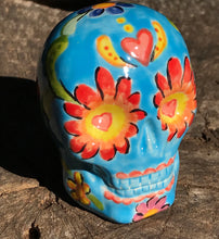 Load image into Gallery viewer, Inspired by nature, this ceramic skull statuette is full of vibrant color and intricate details. The primary color is sky blue with Multi-color floral motifs that are painted across the skull, along with hearts and leaves and lively colorful accents around the entire skull. 
