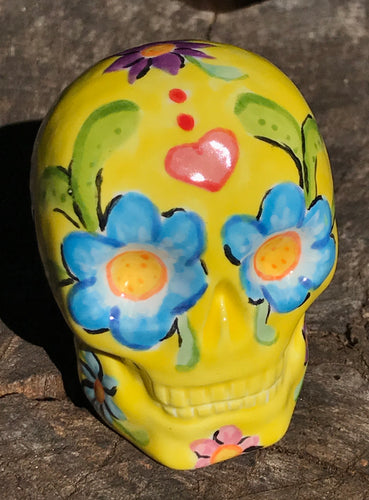 Inspired by nature, this ceramic skull statuette is full of vibrant color and intricate details. The primary color is yellow with Multi-color floral motifs that are painted across the skull, along with hearts and leaves and lively colorful accents around the entire skull.