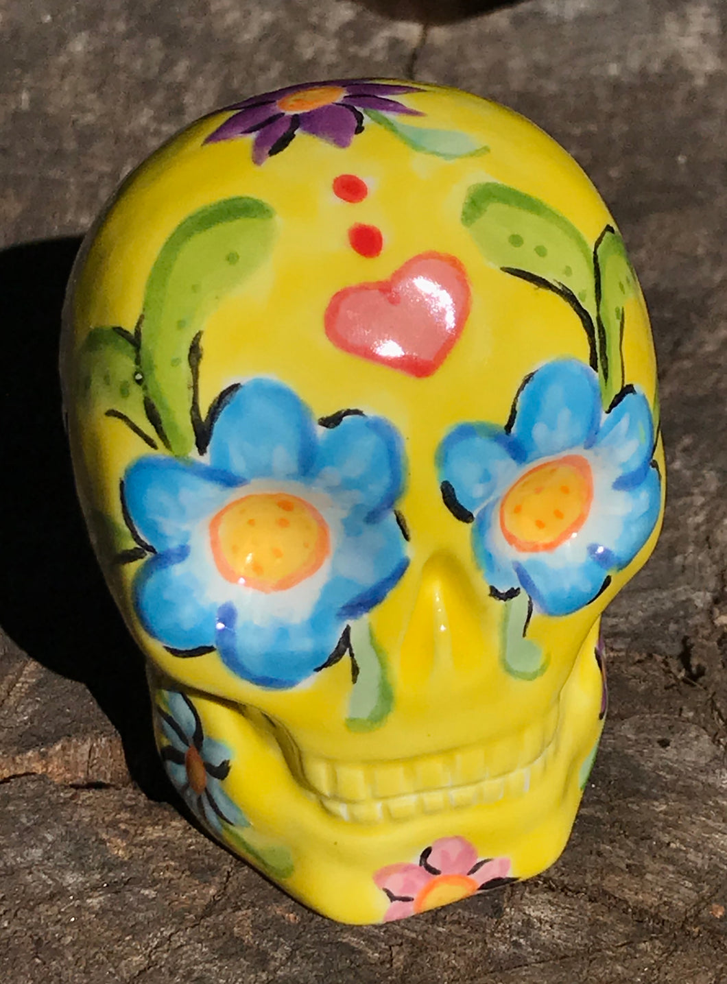 Inspired by nature, this ceramic skull statuette is full of vibrant color and intricate details. The primary color is yellow with Multi-color floral motifs that are painted across the skull, along with hearts and leaves and lively colorful accents around the entire skull.