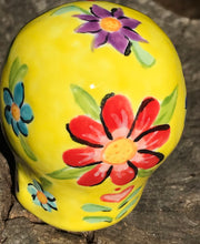 Load image into Gallery viewer,  Inspired by nature, this ceramic skull statuette is full of vibrant color and intricate details. The primary color is yellow with Multi-color floral motifs that are painted across the skull, along with hearts and leaves and lively colorful accents around the entire skull.
