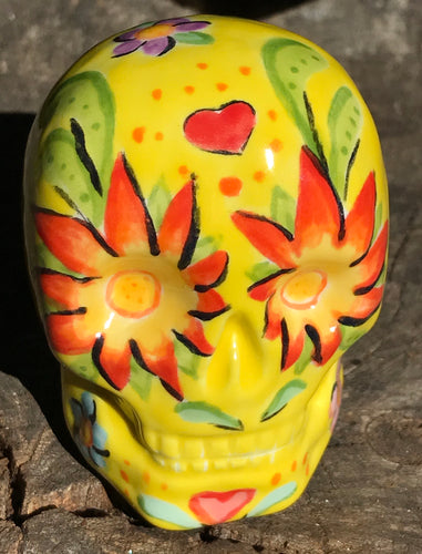 This ceramic skull statuette is a stunning piece of art inspired by nature. Its vibrant yellow hue is decorated with multi-color floral motifs, hearts, leaves and colorful accents, creating a beautiful piece of hand-painted, Day of the Dead-themed art. Measurements: H 2 3/4” x W 2” x D 2”