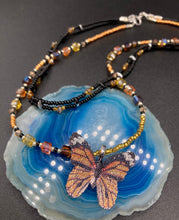 Load image into Gallery viewer, Sterling silver butterfly pendant is molded from a basil leaf and is painted in strikingly bright orange and black.  The first two strands contain two-hole black and silver beads to retain a more &quot;collar&quot; shape. They are primarily black beads with larger orange beads. The third and slightly longer strand has bright gold and orange square shaped glass beads along the black beads to compliment the monarch butterfly wings. Perfect for your summer look! Necklace is 14” adjustable up to 18&quot; - pendant is 1” 

