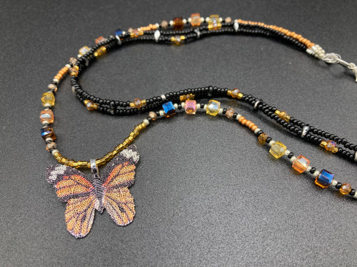Sterling silver butterfly pendant is molded from a basil leaf and is painted in strikingly bright orange and black.  The first two strands contain two-hole black and silver beads to retain a more 