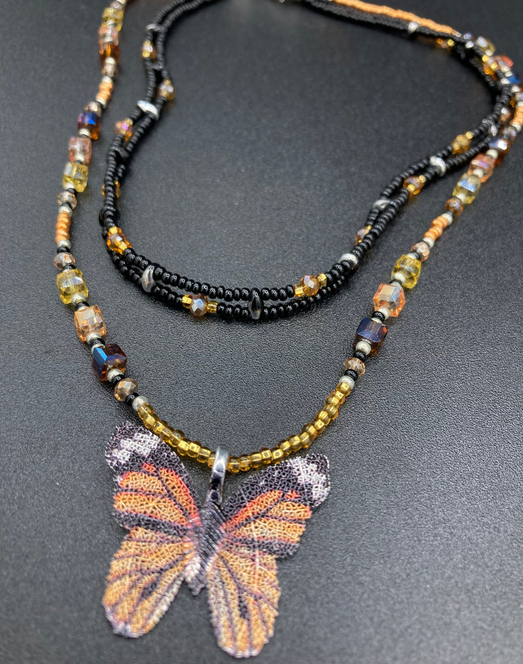 Sterling silver butterfly pendant is molded from a basil leaf and is painted in strikingly bright orange and black.  The first two strands contain two-hole black and silver beads to retain a more 