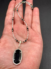 Load image into Gallery viewer, This dainty necklace is full of black and silver shimmery glass beads. A length black oval shaped glass bead hangs low to add length to this necklace.  It&#39;s the perfect necklace to add a little elegance to any outfit. Will go with any outfit, dress it up or down, this necklace will complete any look. This beauty is a must-have, add it to your jewelry collection.  Measurements: Necklace is 15 1/2” adjustable up to 18&quot;- pendant is 1 1/2” Height
